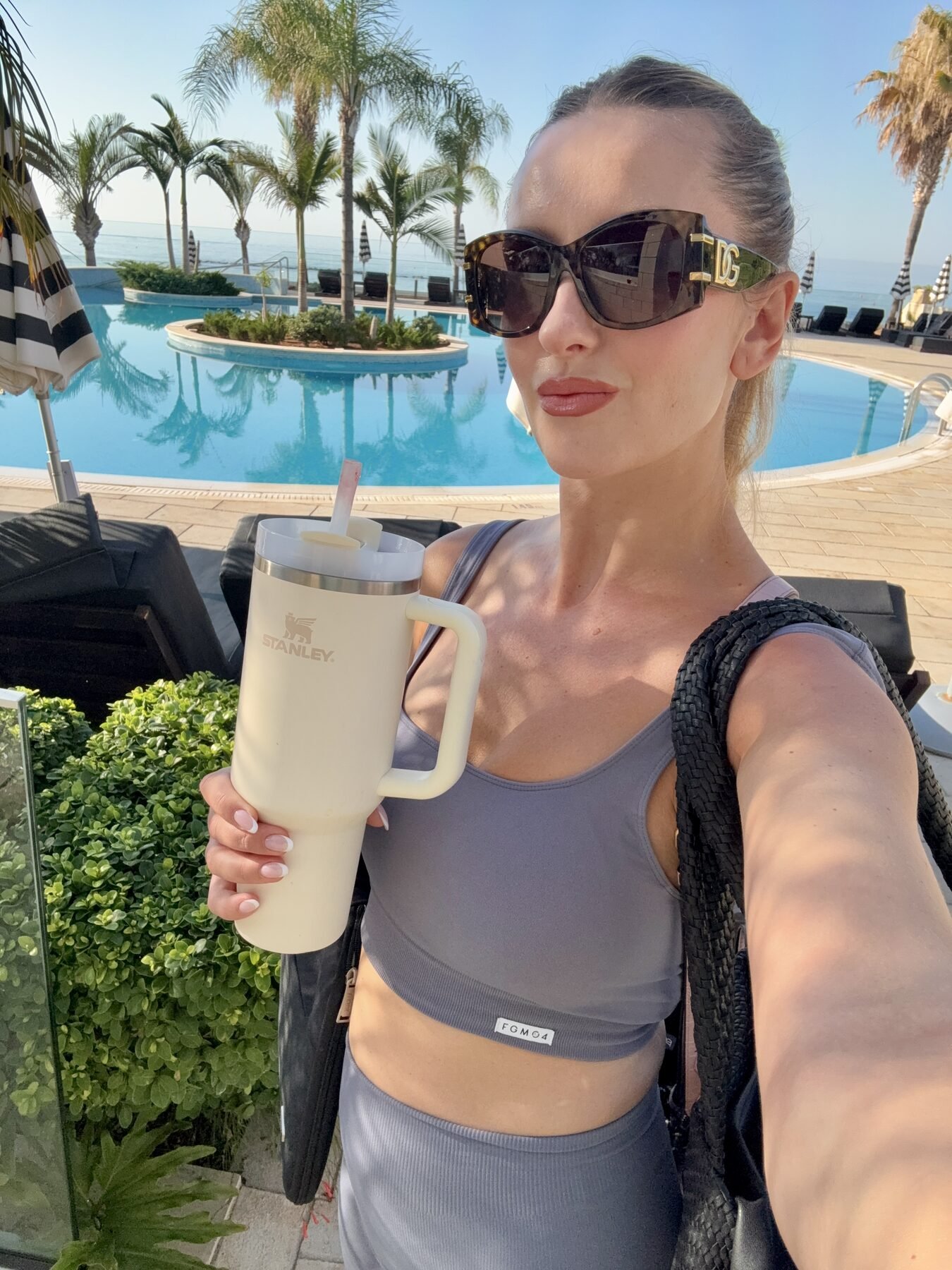 Cream Stanley Quencher travel tumbler held by a woman at a luxury beachfront pool.
